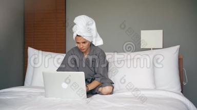 年轻的白种人女士在酒店房间里坐在床上时使用笔记本电脑